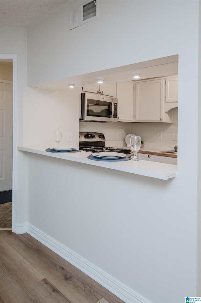 kitchen featuring a textured ceiling, kitchen peninsula, stainless steel appliances, light hardwood / wood-style floors, and white cabinets