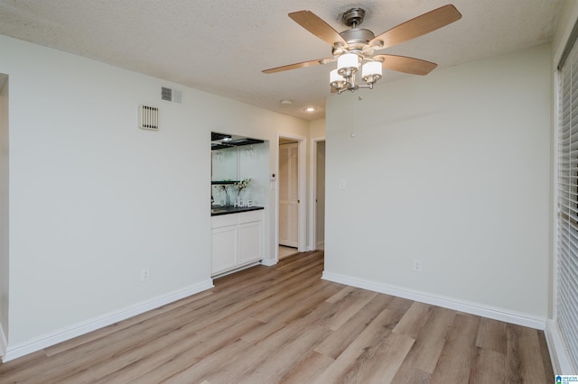 empty room with ceiling fan, light hardwood / wood-style flooring, and a textured ceiling