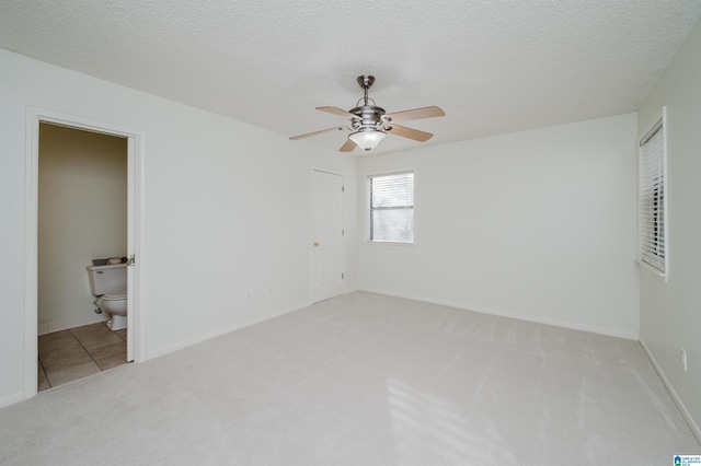 unfurnished bedroom featuring ceiling fan, light colored carpet, ensuite bathroom, and a textured ceiling