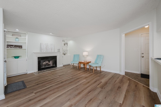 sitting room with built in shelves, a textured ceiling, and light hardwood / wood-style floors