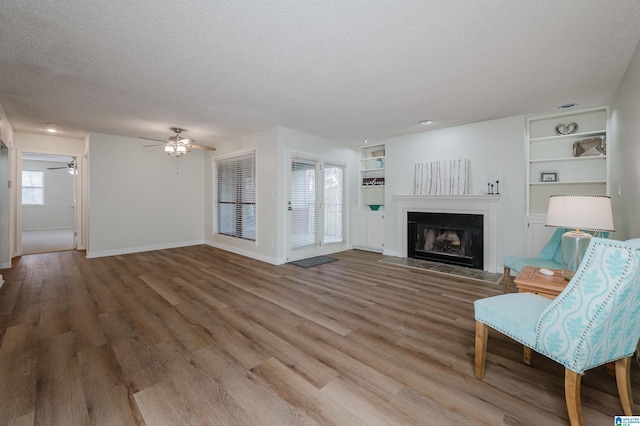 unfurnished living room with built in shelves, ceiling fan, wood-type flooring, and a textured ceiling