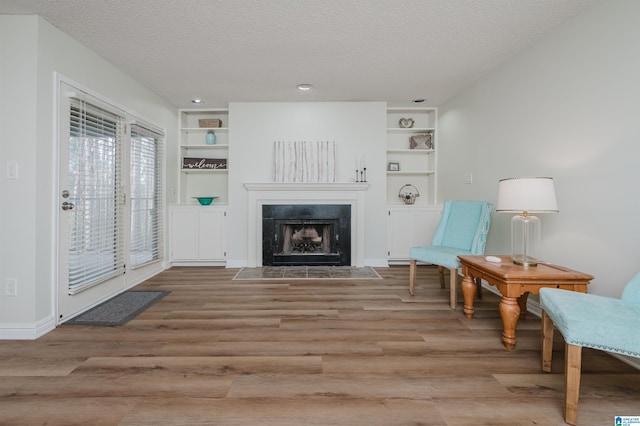 sitting room with built in shelves, light hardwood / wood-style flooring, and a textured ceiling