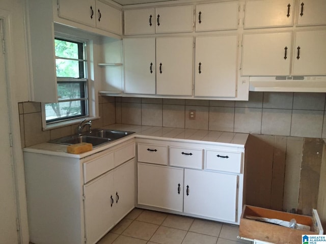 kitchen with sink, light tile patterned floors, tile counters, white cabinets, and decorative backsplash