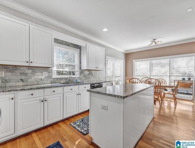 kitchen featuring crown molding, white cabinetry, a center island, light stone counters, and light wood-type flooring