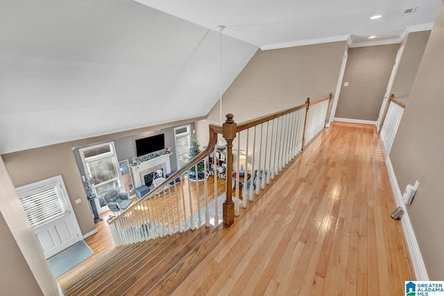 corridor with ornamental molding, lofted ceiling, and hardwood / wood-style floors