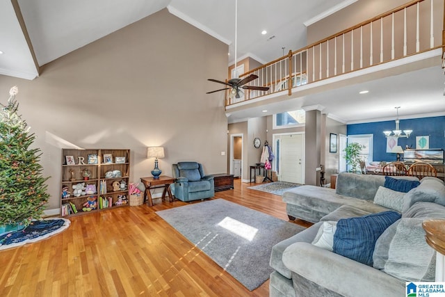 living room with crown molding, a towering ceiling, ceiling fan with notable chandelier, and hardwood / wood-style flooring