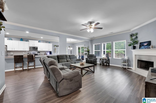 living room featuring crown molding, dark hardwood / wood-style flooring, a tiled fireplace, and ceiling fan with notable chandelier