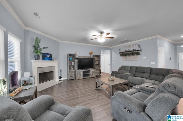 living room with hardwood / wood-style flooring, a tiled fireplace, ornamental molding, and ceiling fan