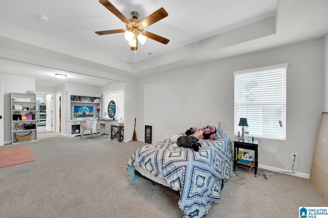 carpeted bedroom with ceiling fan and a tray ceiling