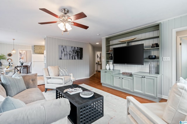 living room with ornamental molding, ceiling fan, and light wood-type flooring