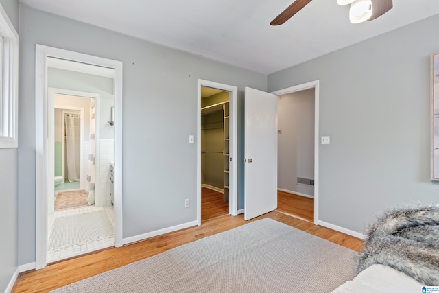 bedroom with hardwood / wood-style flooring, a walk in closet, connected bathroom, and ceiling fan