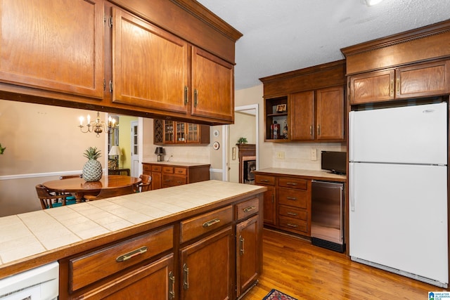 kitchen with decorative light fixtures, white refrigerator, tile counters, light hardwood / wood-style floors, and backsplash