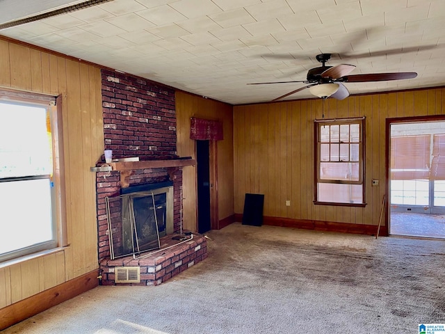 unfurnished living room featuring ceiling fan, a brick fireplace, light carpet, and wood walls