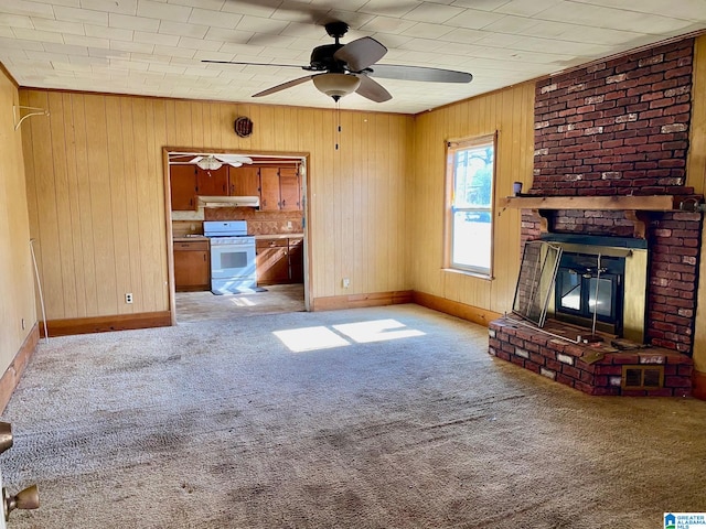 unfurnished living room with ceiling fan, light colored carpet, wooden walls, and a brick fireplace