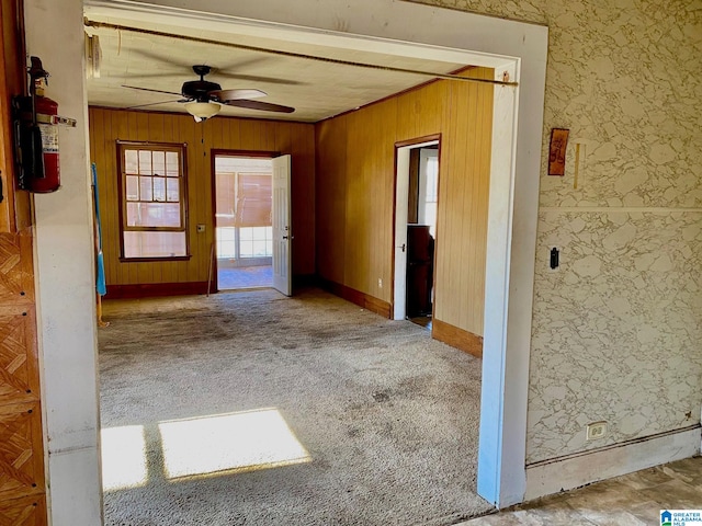 carpeted empty room with ceiling fan and wood walls