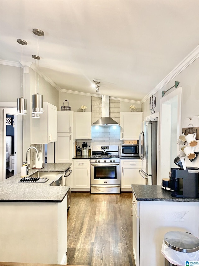 kitchen with sink, appliances with stainless steel finishes, white cabinetry, decorative light fixtures, and wall chimney exhaust hood