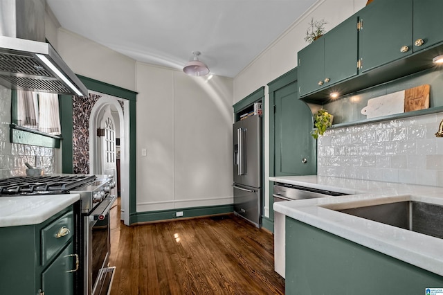 kitchen with dark wood-type flooring, backsplash, premium appliances, green cabinetry, and wall chimney exhaust hood