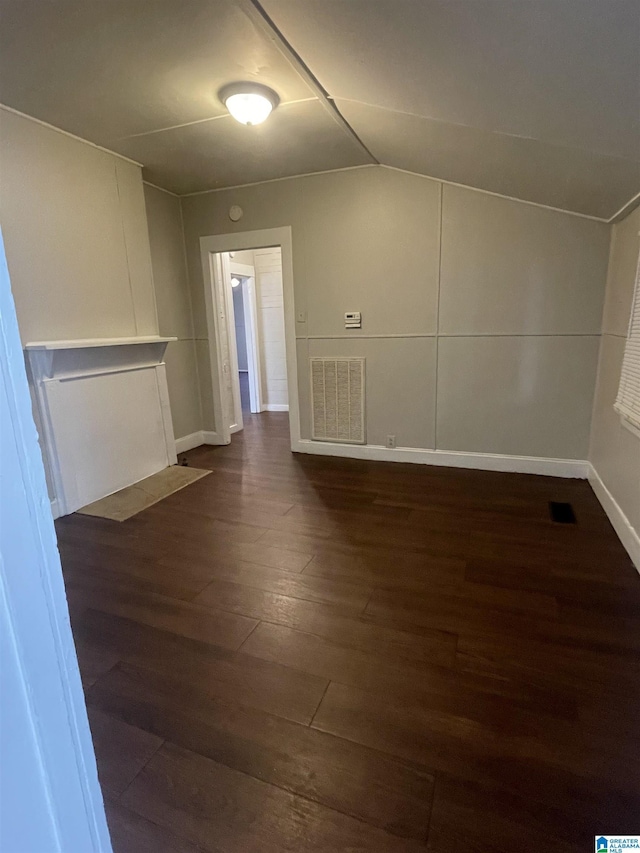 unfurnished room with dark wood-style floors, vaulted ceiling, visible vents, and baseboards