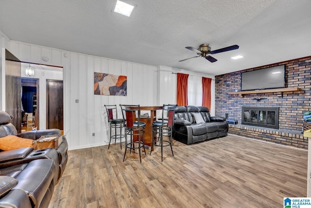 living room featuring wood-type flooring, a brick fireplace, ceiling fan, and a textured ceiling