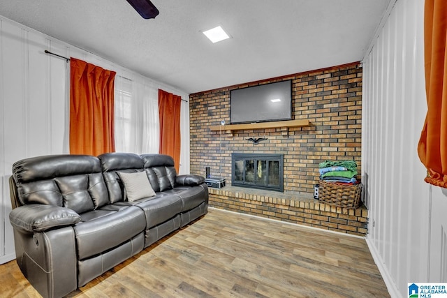 living room with brick wall, a fireplace, hardwood / wood-style flooring, ceiling fan, and a textured ceiling