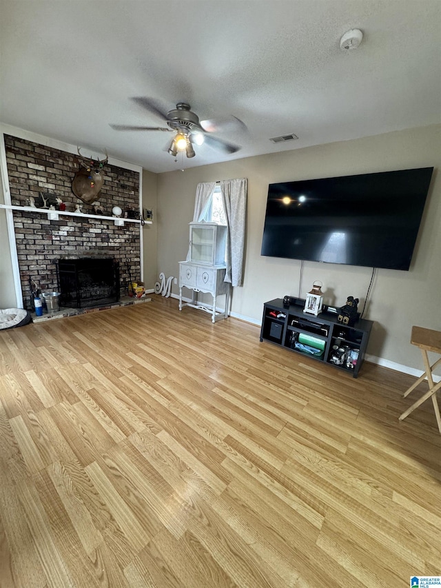 living room featuring a brick fireplace, light hardwood / wood-style floors, a textured ceiling, and ceiling fan