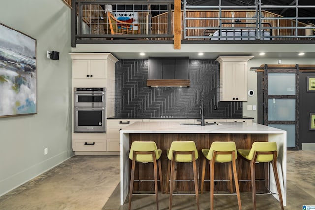 kitchen with white cabinetry, a barn door, an island with sink, and double oven