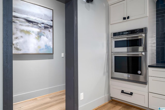 kitchen featuring stainless steel double oven, light hardwood / wood-style floors, and white cabinets