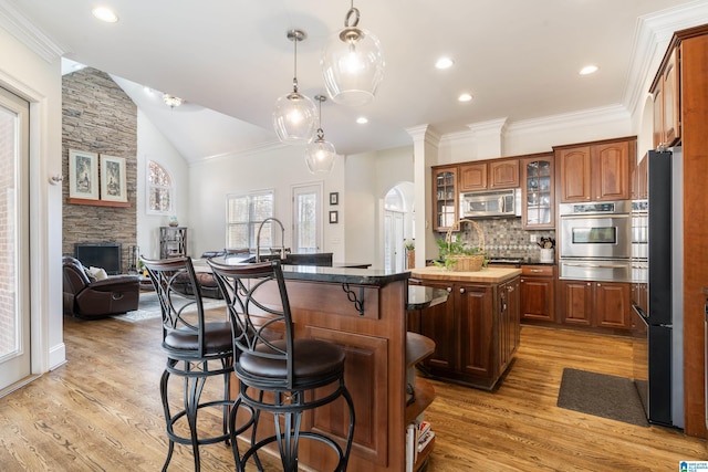 kitchen featuring appliances with stainless steel finishes, a breakfast bar, a fireplace, hanging light fixtures, and a kitchen island with sink