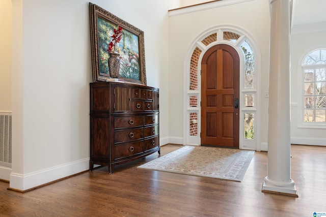 foyer featuring wood-type flooring, ornamental molding, and ornate columns