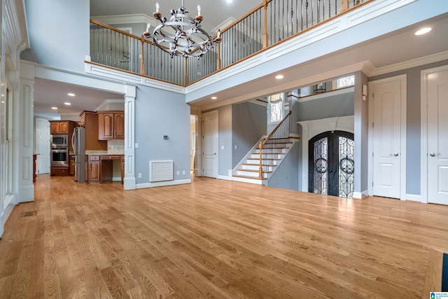 unfurnished living room with a high ceiling, crown molding, a notable chandelier, and light wood-type flooring