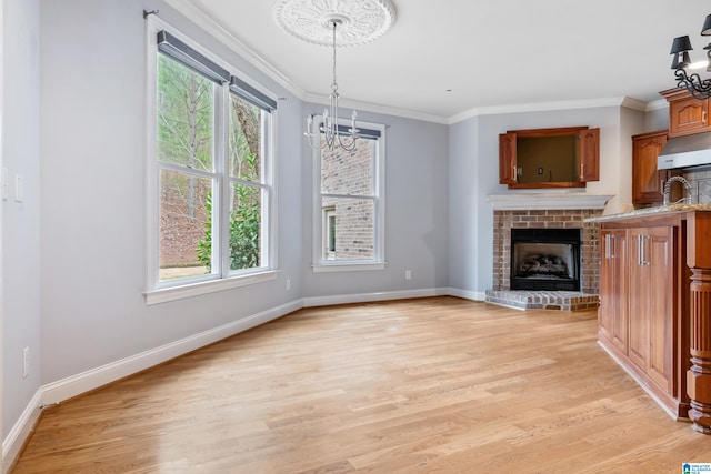 unfurnished living room featuring crown molding, an inviting chandelier, a brick fireplace, and light wood-type flooring