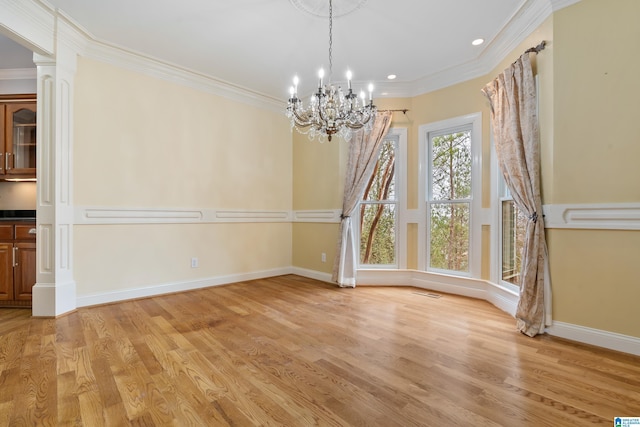 unfurnished dining area with a notable chandelier, crown molding, ornate columns, and light wood-type flooring