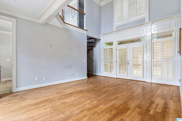 unfurnished living room with crown molding, light hardwood / wood-style flooring, french doors, and a towering ceiling