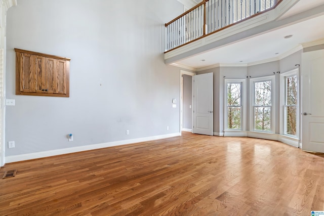 unfurnished living room featuring a high ceiling, ornamental molding, and light hardwood / wood-style floors