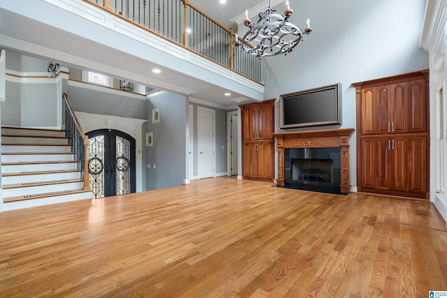 unfurnished living room featuring light hardwood / wood-style flooring, a high ceiling, ornamental molding, french doors, and a chandelier