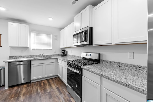 kitchen with appliances with stainless steel finishes, dark hardwood / wood-style floors, white cabinetry, sink, and light stone countertops