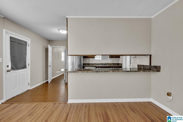 kitchen featuring a textured ceiling, stainless steel refrigerator, ornamental molding, kitchen peninsula, and hardwood / wood-style flooring