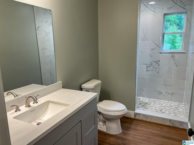 bathroom featuring hardwood / wood-style flooring, vanity, tiled shower, and toilet