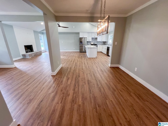 unfurnished living room with an inviting chandelier, a brick fireplace, light hardwood / wood-style flooring, and ornamental molding