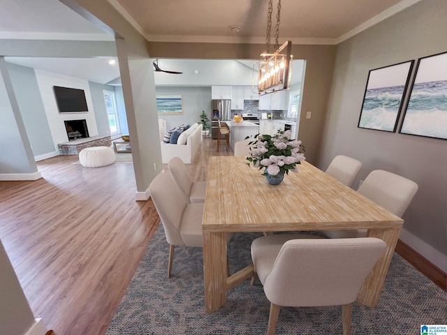 dining room with a notable chandelier, wood-type flooring, ornamental molding, and a large fireplace