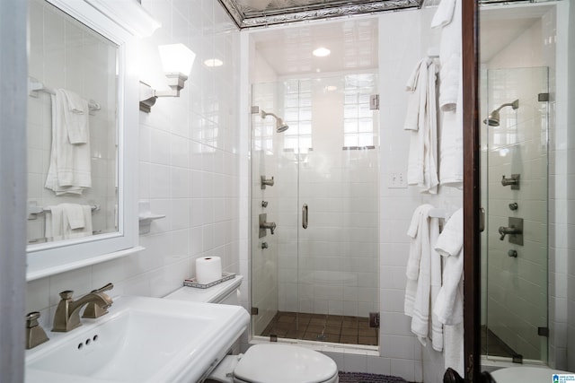 bathroom with a shower with shower door, tasteful backsplash, sink, tile walls, and toilet