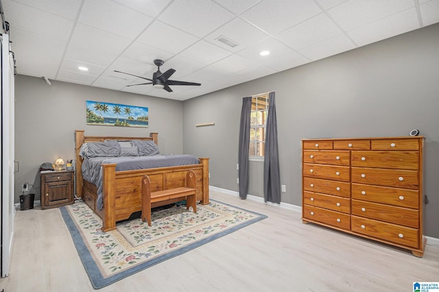 bedroom with a drop ceiling, ceiling fan, and light hardwood / wood-style flooring