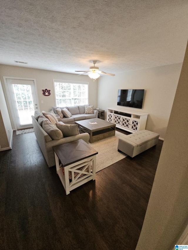 living room with dark wood-type flooring, ceiling fan, and a textured ceiling