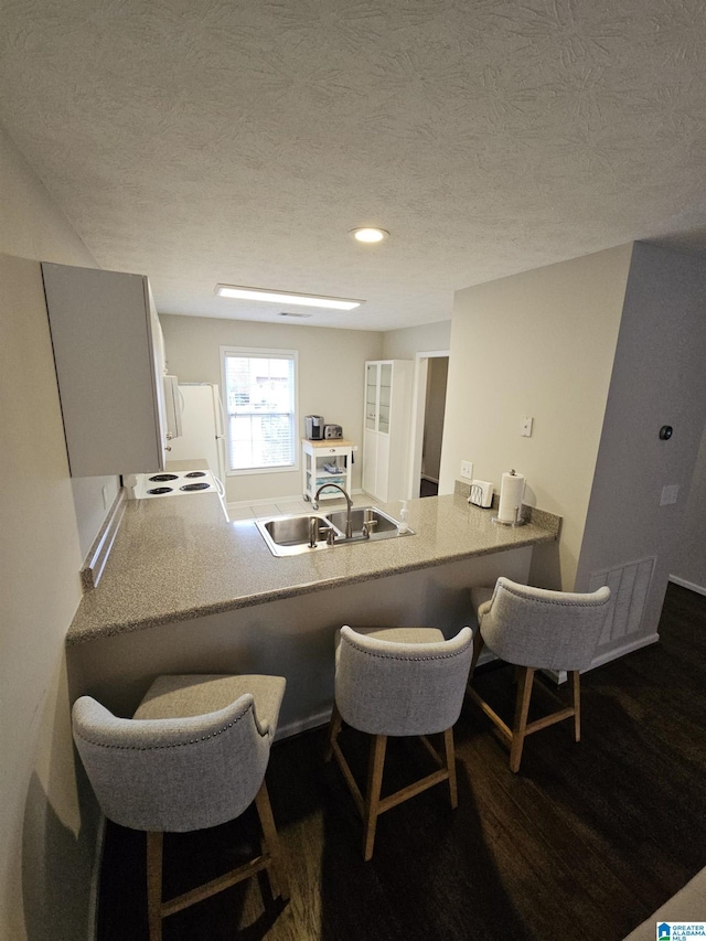 kitchen with a breakfast bar, wood-type flooring, sink, kitchen peninsula, and a textured ceiling