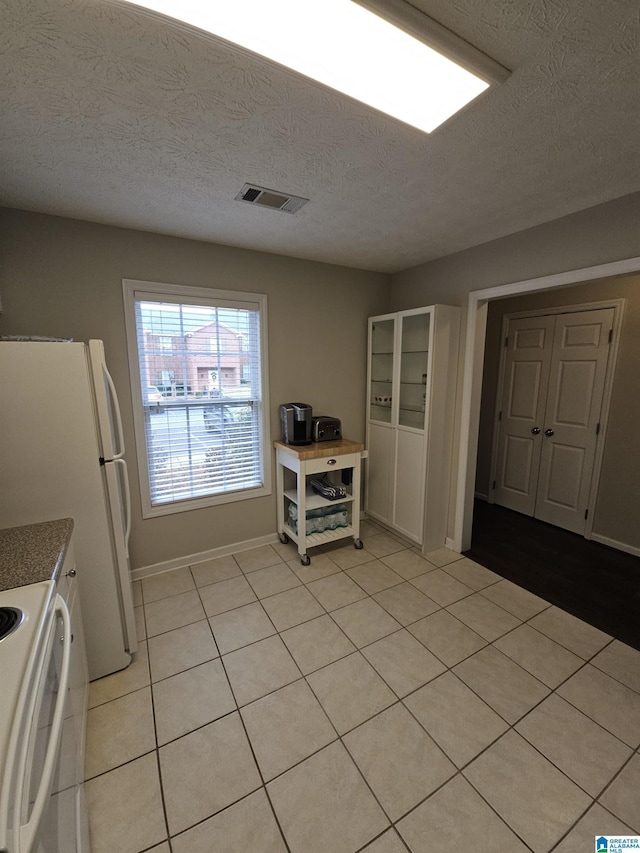 kitchen featuring range, white refrigerator, a textured ceiling, light tile patterned flooring, and white cabinets