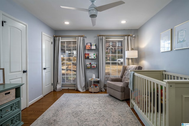 bedroom featuring wood-type flooring, a nursery area, and ceiling fan