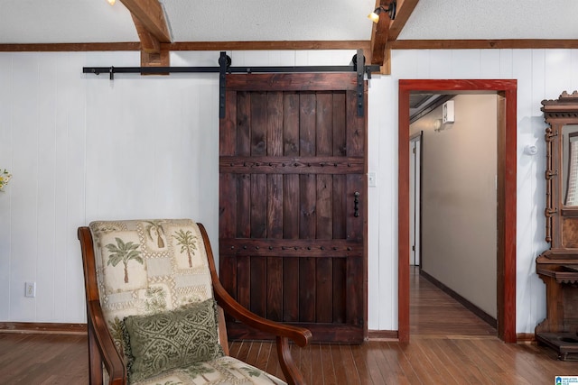 sitting room featuring a textured ceiling, wood-type flooring, a barn door, and beamed ceiling