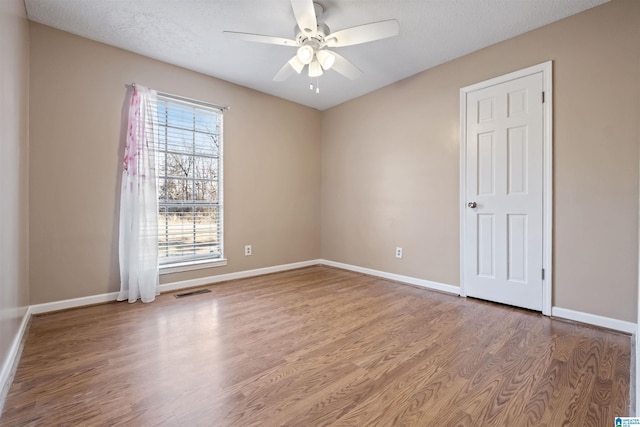 unfurnished room featuring visible vents, wood finished floors, a ceiling fan, and baseboards