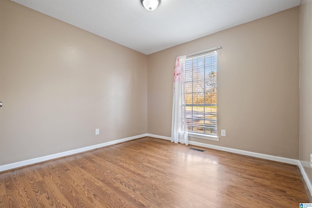 unfurnished room featuring light wood-style flooring, visible vents, baseboards, and a textured ceiling