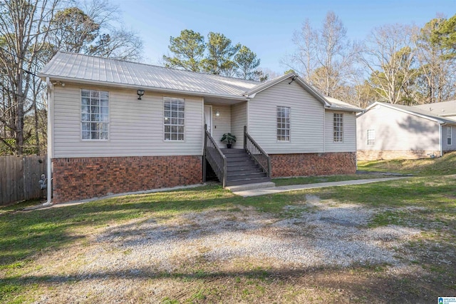 view of front of property featuring fence, a front lawn, metal roof, and brick siding